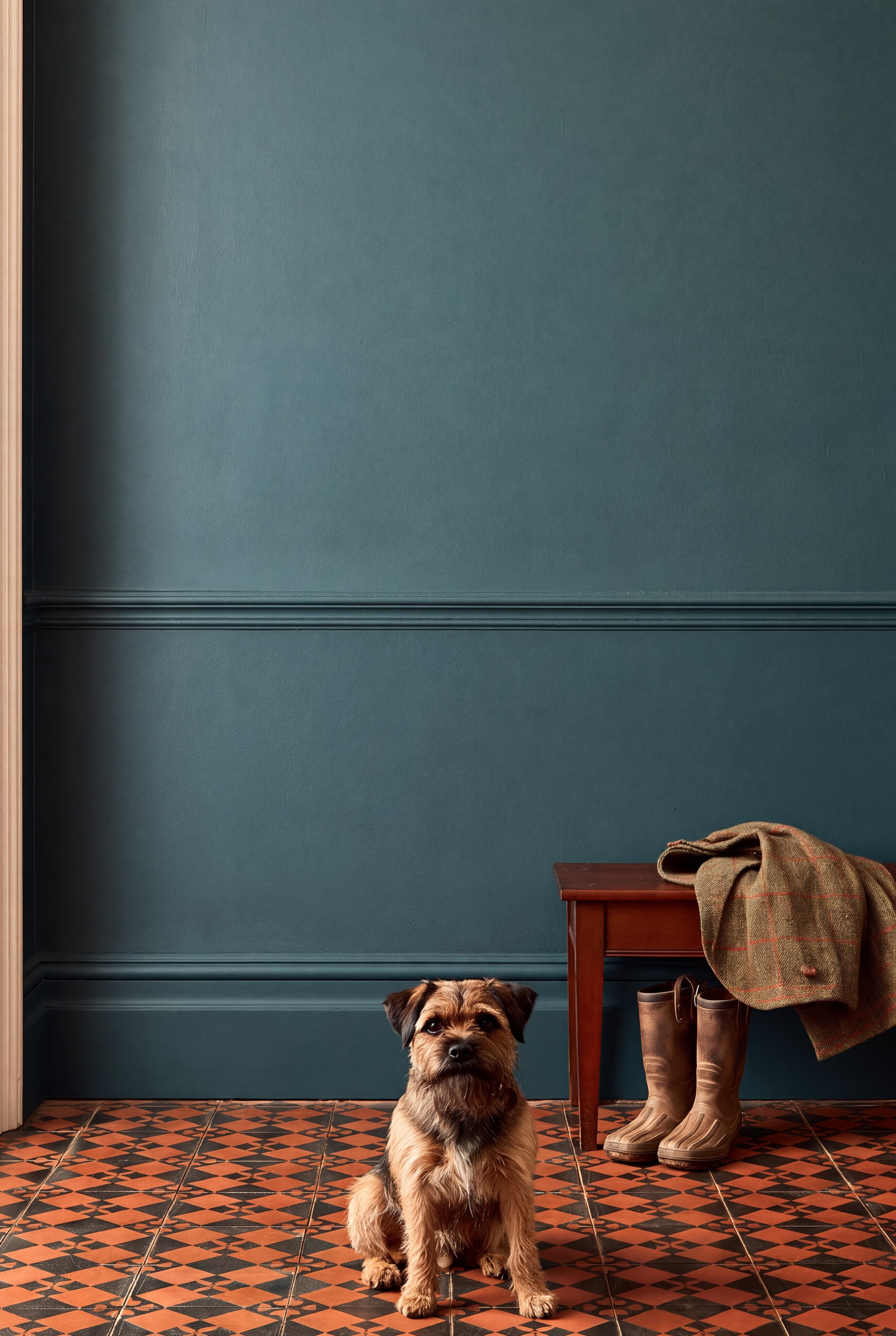 Victorian hallway with a deep teal wall above a dado rail, encaustic tile floor, hall bench with boots, and a Border terrier, ranked 10 among 11x17 poster mockups