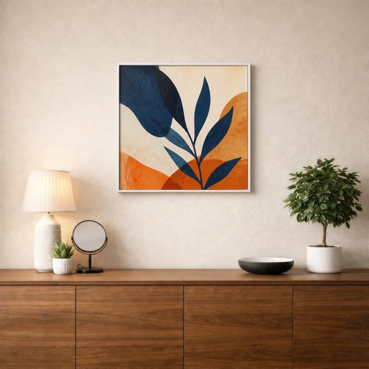 Square indigo and orange botanical abstract in a white frame beside a potted tree