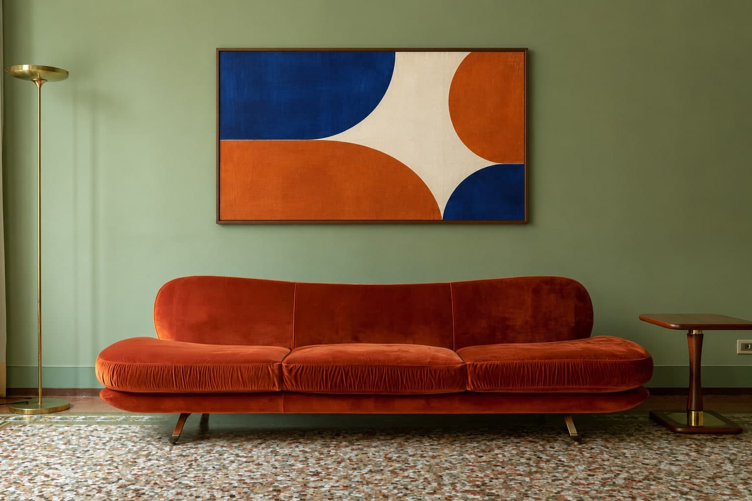Cobalt, ivory, and burnt orange geometric art in a walnut frame above a rust sofa on a green Milan living-room wall