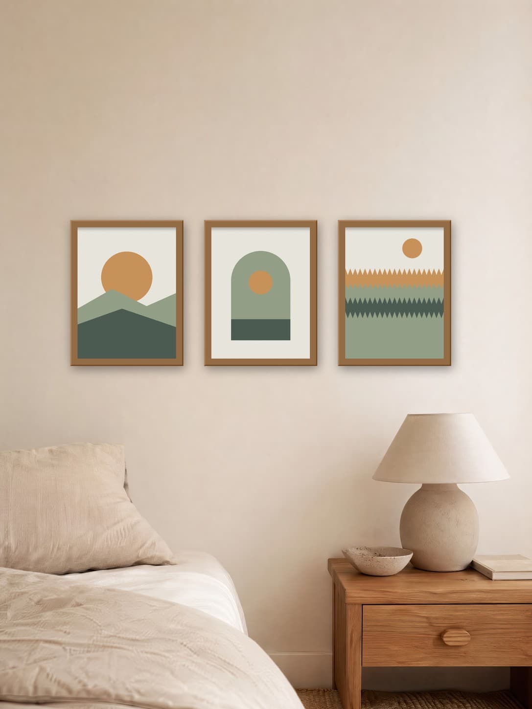 Three sage and ochre landscape posters in oak frames on a linen bedroom wall above a nightstand