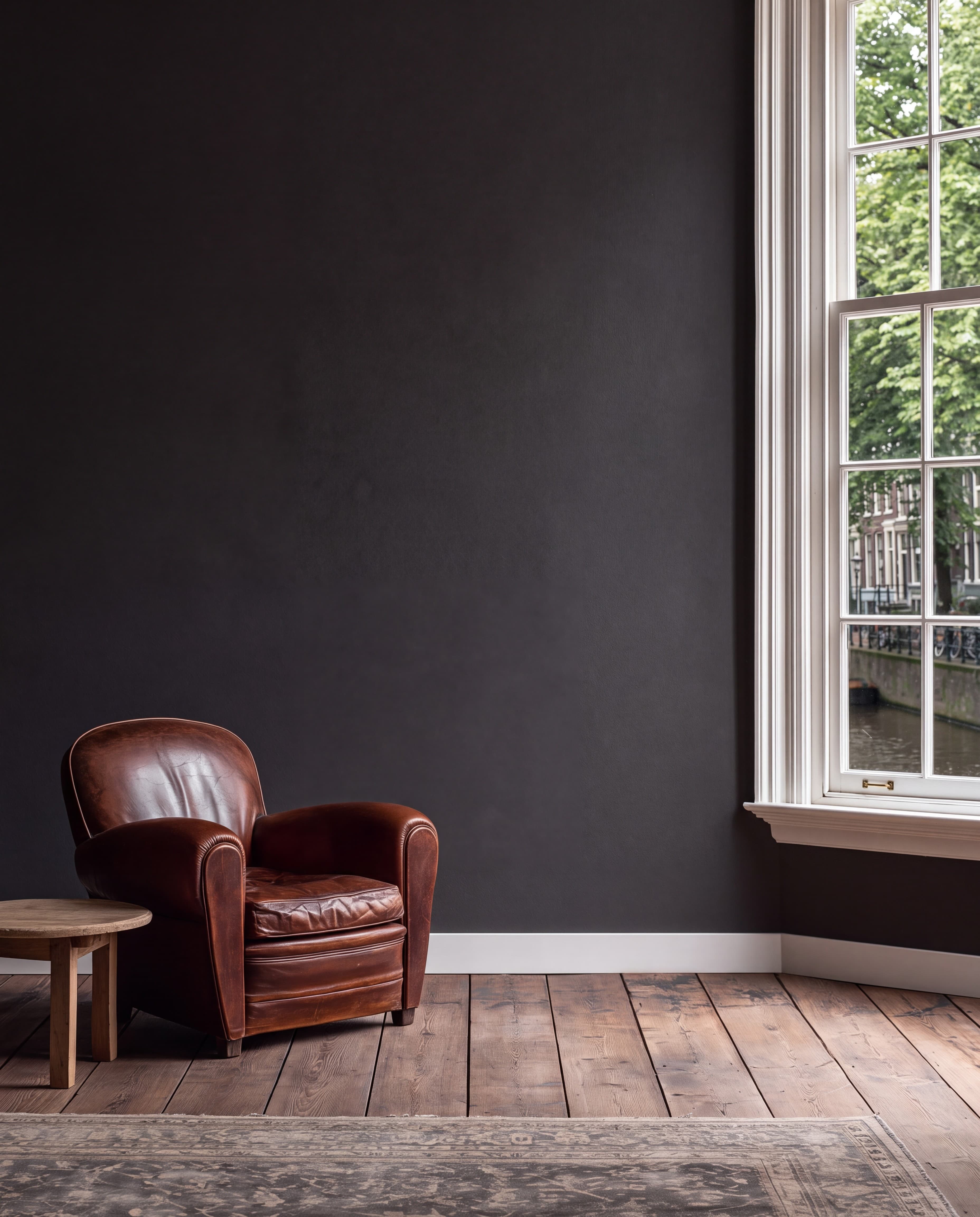 Amsterdam canal house living room with a deep charcoal wall, leather club chair, tall sash window, and old oak floorboards, ranked 11 among european room mockups