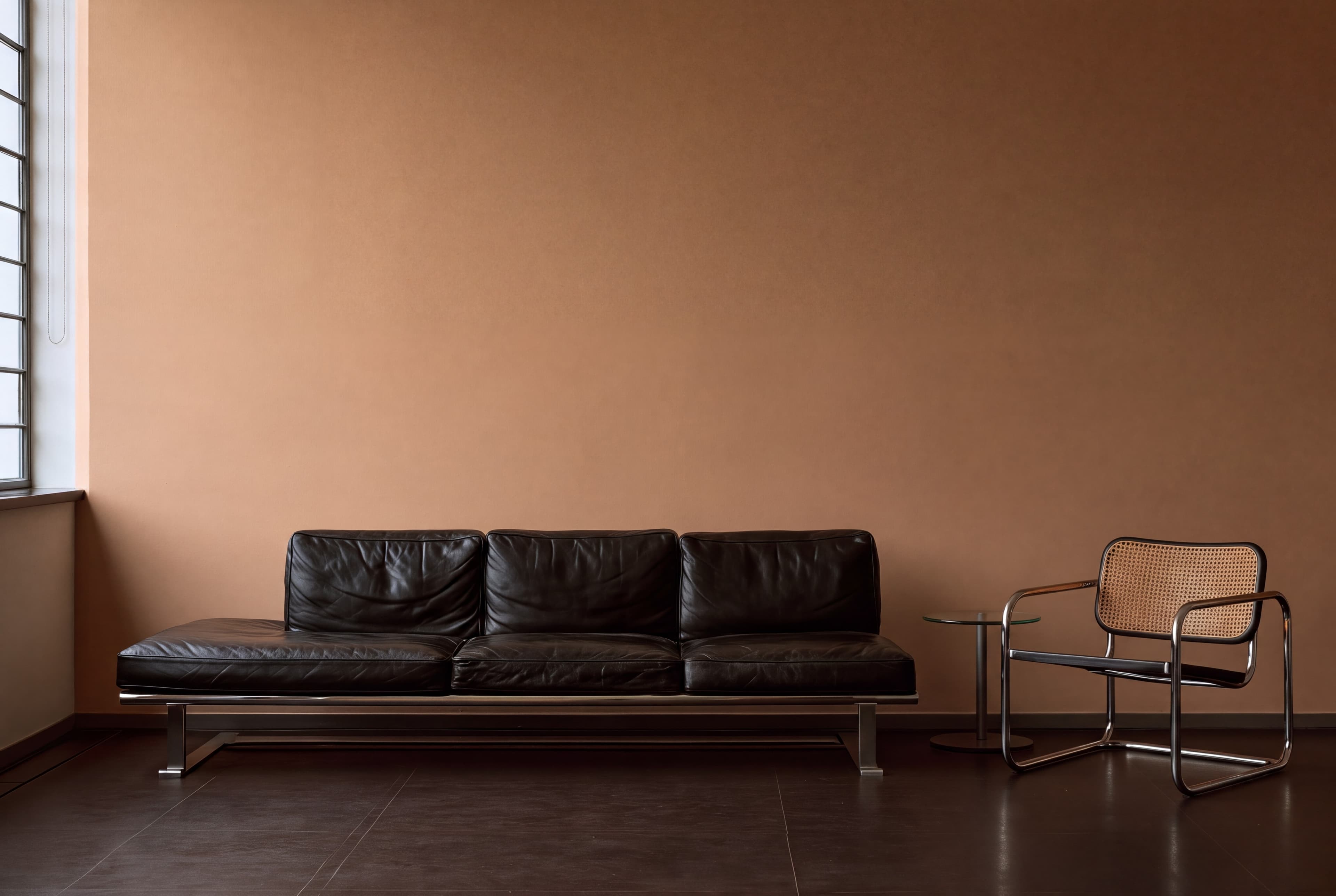 Bauhaus-inspired living room with a warm tan wall, black leather sofa on a chrome frame, and tubular steel cane chair, ranked 5 among european room mockups