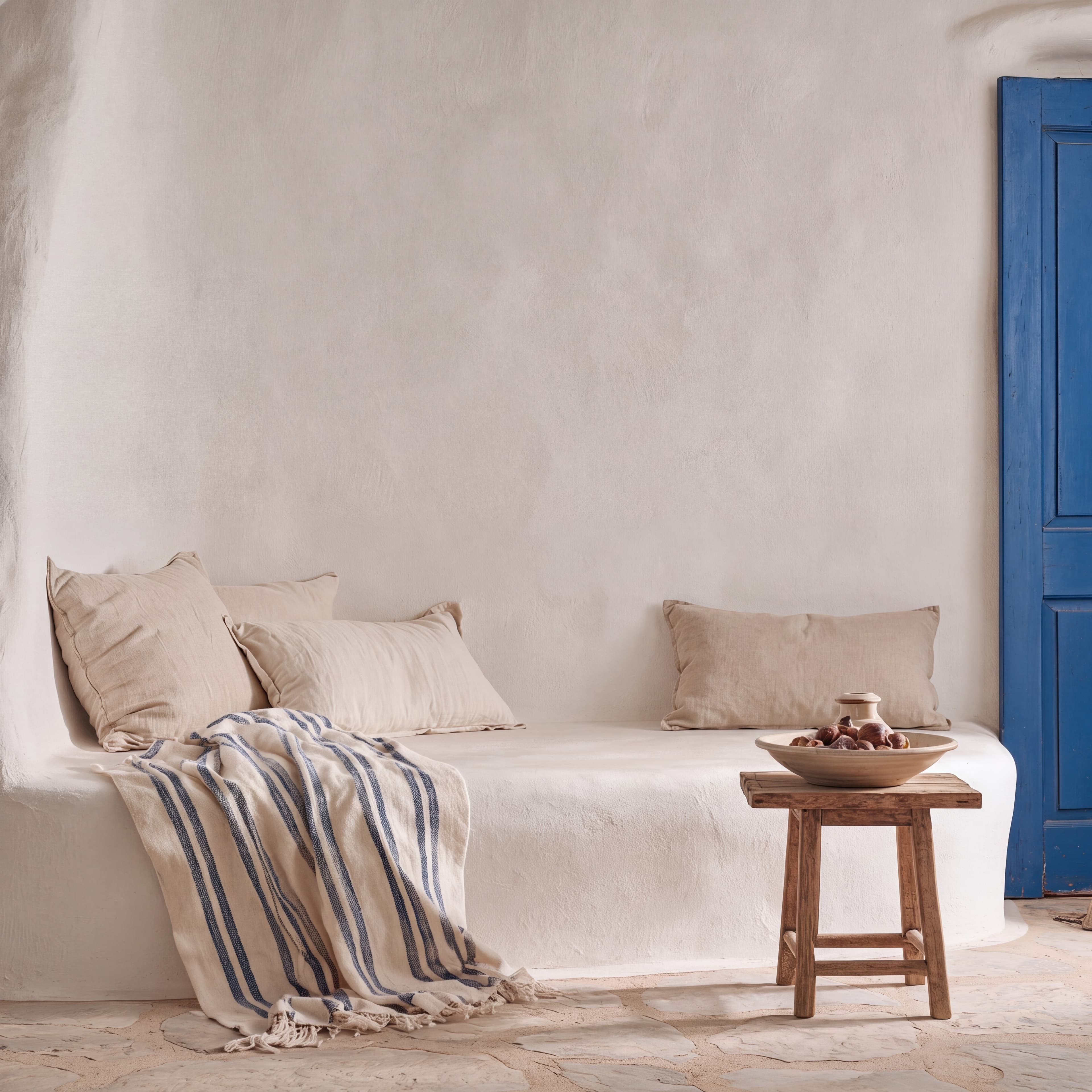 Greek island living room with a whitewashed wall, built-in banquette with linen cushions, striped throw, and blue door, ranked 17 among european room mockups