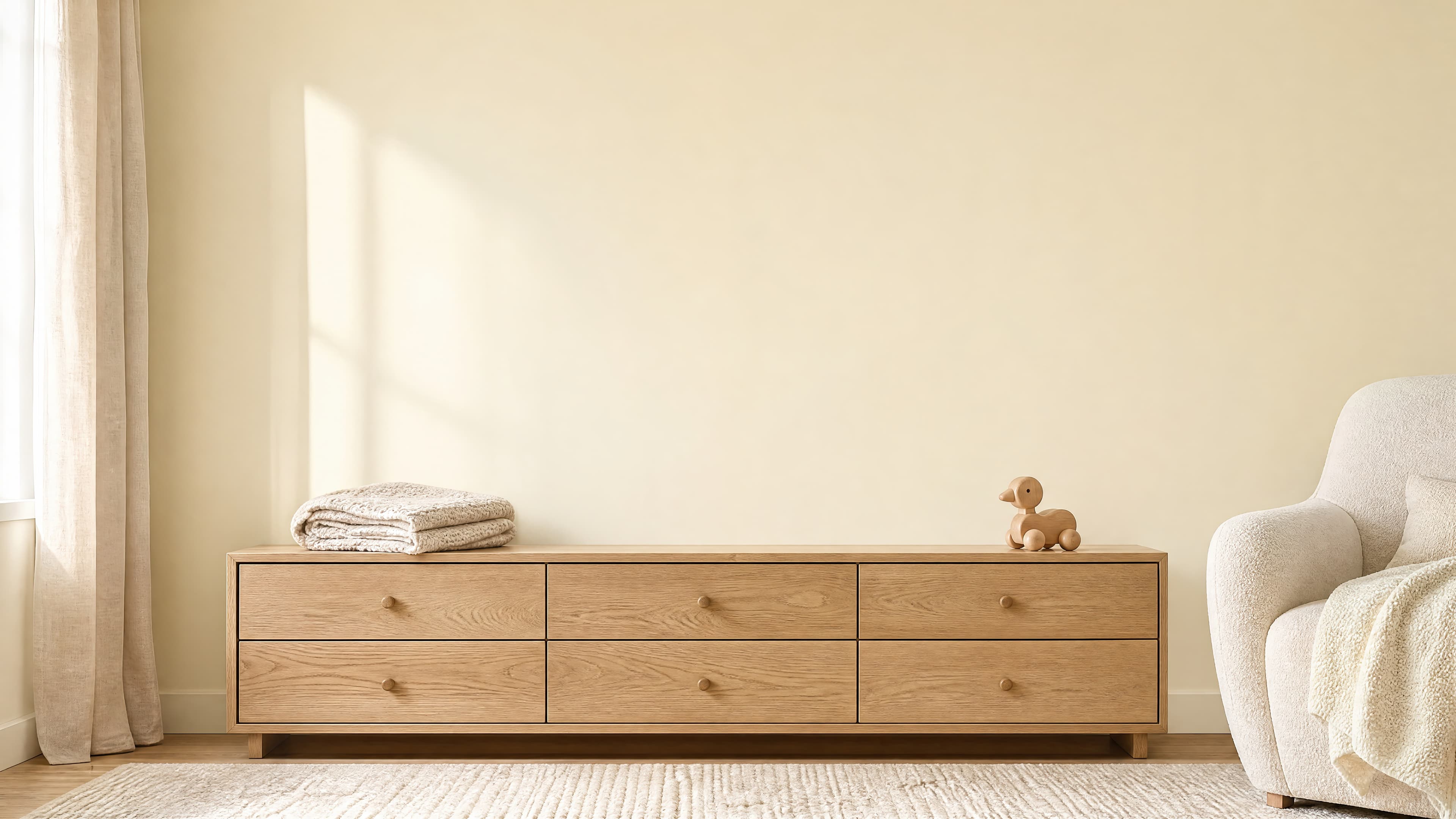 Soft Scandinavian nursery with a pale yellow wall above a long oak dresser and a cream boucle chair, ranked 7 among nursery mockups