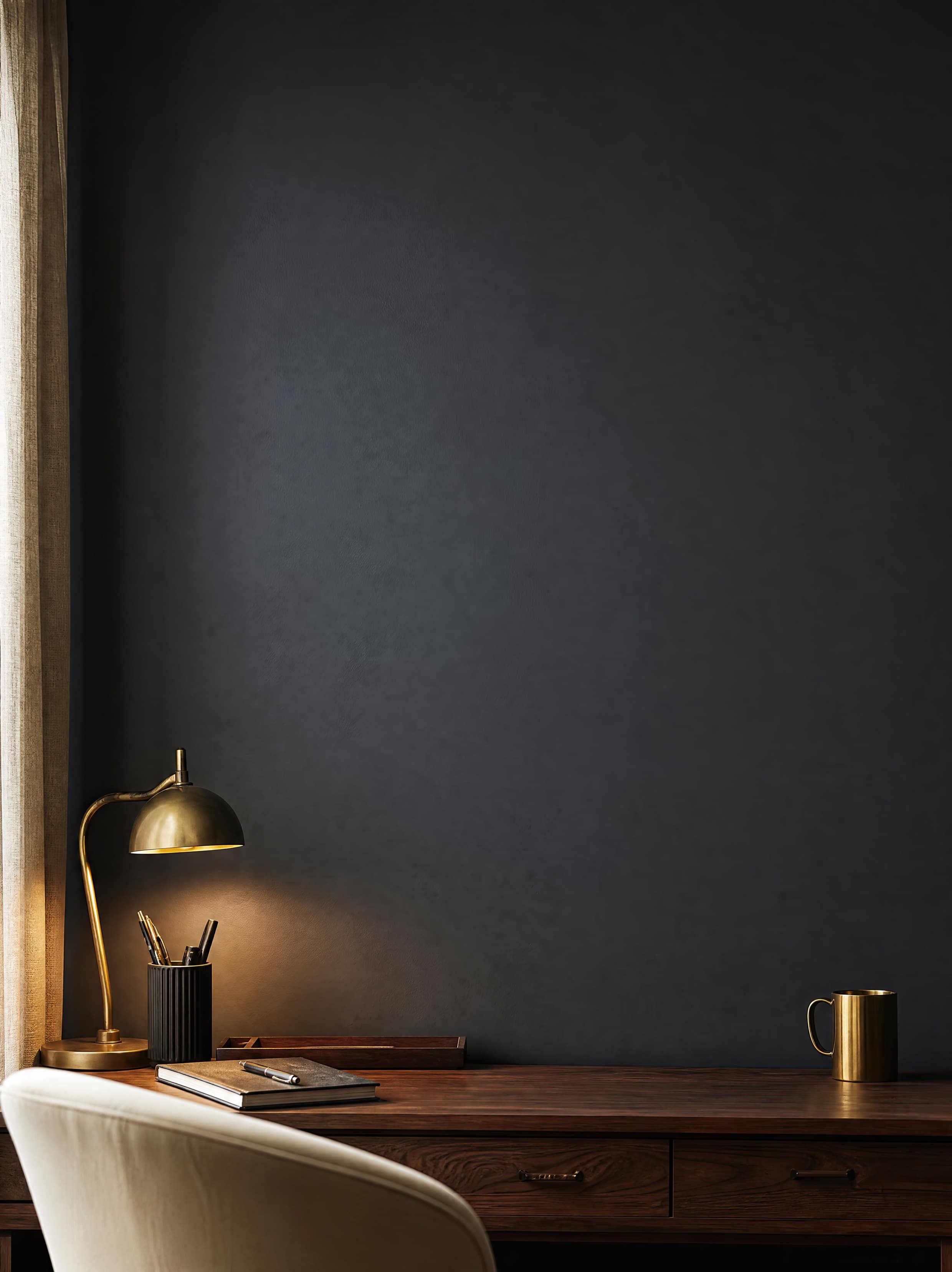 Moody office nook with an empty charcoal plaster wall above a walnut desk and brass accents, selected for office mockups