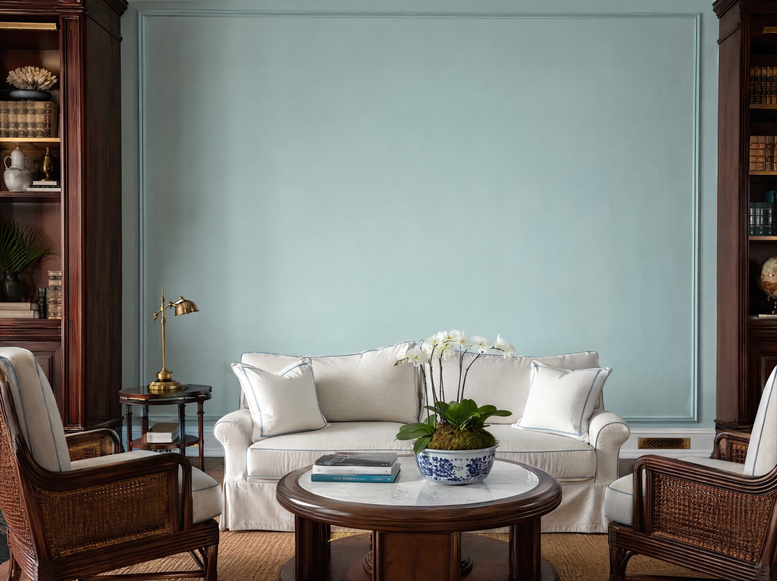 Pale blue-green display wall framed by mahogany bookcases in the Bahamian colonial library room
