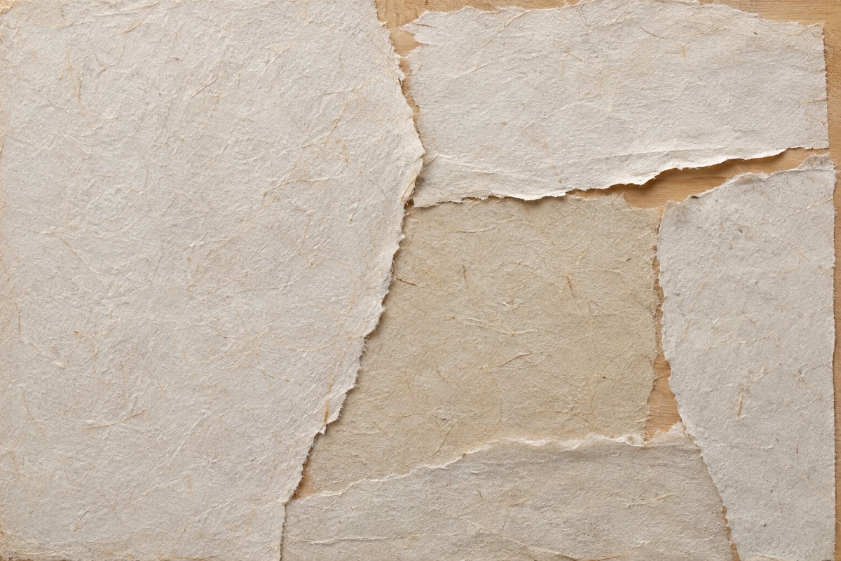 Overhead process crop of torn paper firmly adhered to a square wood panel with three raised deckled edges before glazing