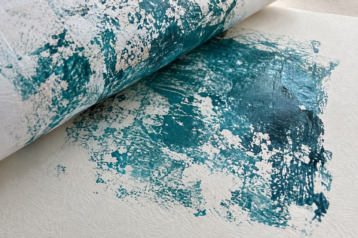 Close overhead process view of a painted donor sheet being partially lifted to reveal a broken teal acrylic transfer